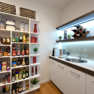 Modern kitchen pantry ideas - Example of a minimalist galley light wood floor kitchen pantry design in Newcastle - Maitland with an undermount sink, flat-panel cabinets, white cabinets, quartz countertops, metallic backsplash, glass sheet backsplash and an island