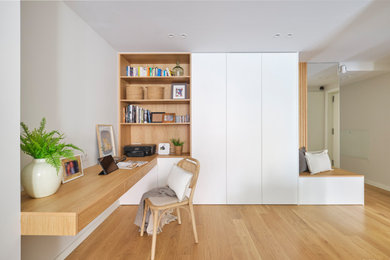 Modelo de despacho escandinavo de tamaño medio con paredes blancas, suelo de madera en tonos medios, escritorio empotrado y suelo marrón