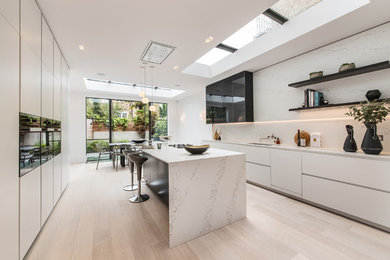 Photo of a mid-sized contemporary galley eat-in kitchen in London with flat-panel cabinets, white cabinets, white splashback, marble splashback, light hardwood floors, with island, beige floor and marble benchtops.