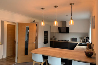 Photo of a mid-sized contemporary u-shaped eat-in kitchen in Other with a double-bowl sink, flat-panel cabinets, grey cabinets, laminate benchtops, grey splashback, glass sheet splashback, panelled appliances, vinyl floors, a peninsula, grey floor and brown benchtop.