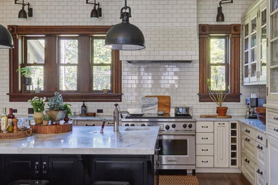This is an example of a large transitional kitchen in Chicago with an undermount sink, recessed-panel cabinets, white cabinets, marble benchtops, white splashback, subway tile splashback, white appliances, dark hardwood floors, with island, brown floor and white benchtop.