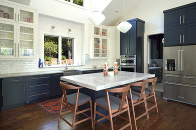 Inspiration for a transitional l-shaped medium tone wood floor and brown floor kitchen remodel in Other with a farmhouse sink, shaker cabinets, blue cabinets, white backsplash, subway tile backsplash, stainless steel appliances, an island and gray countertops