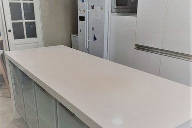 Inspiration for a medium sized modern single-wall enclosed kitchen in London with a submerged sink, flat-panel cabinets, white cabinets, quartz worktops, white splashback, glass tiled splashback, stainless steel appliances, ceramic flooring, an island, beige floors, white worktops, a coffered ceiling and feature lighting.