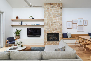Großes Modernes Wohnzimmer mit weißer Wandfarbe, Sperrholzboden, Kamin, verputzter Kaminumrandung, TV-Wand und braunem Boden in Sonstige