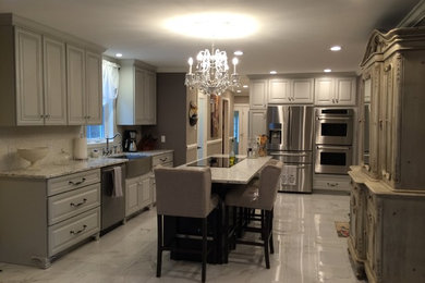 Example of a large classic u-shaped marble floor eat-in kitchen design in New York with a farmhouse sink, raised-panel cabinets, white cabinets, granite countertops, stainless steel appliances and an island