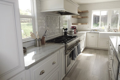 Large cottage l-shaped laminate floor and gray floor eat-in kitchen photo in Santa Barbara with a farmhouse sink, raised-panel cabinets, white cabinets, subway tile backsplash, stainless steel appliances and an island