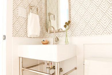 Example of a small transitional light wood floor, brown floor and wallpaper powder room design in Chicago with open cabinets, white cabinets, a one-piece toilet, multicolored walls, a wall-mount sink, white countertops and a freestanding vanity