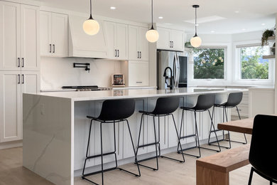 Example of a large transitional galley light wood floor open concept kitchen design in Other with a farmhouse sink, shaker cabinets, white cabinets, quartz countertops, white backsplash, quartz backsplash, stainless steel appliances, an island and white countertops