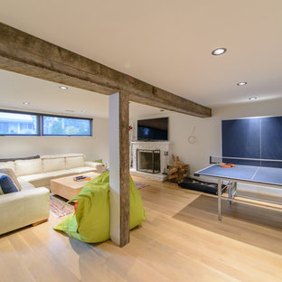 This is an example of an expansive contemporary look-out basement in Toronto with white walls, light hardwood flooring, a standard fireplace and a brick fireplace surround.