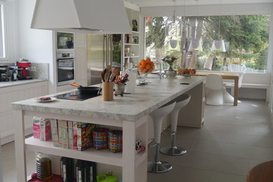 Foto de cocinas en L minimalista extra grande abierta con fregadero bajoencimera, armarios tipo vitrina, puertas de armario blancas, electrodomésticos de acero inoxidable, suelo de baldosas de porcelana, una isla, suelo gris, encimeras blancas, encimera de granito y salpicadero de losas de piedra