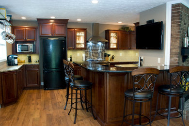 Cette image montre une cuisine minimaliste en bois foncé de taille moyenne avec un placard avec porte à panneau encastré, un plan de travail en granite, une crédence beige, un électroménager noir, un sol en bois brun, une péninsule et un évier encastré.