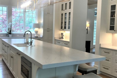 Example of a large minimalist medium tone wood floor and brown floor kitchen design in Miami with a single-bowl sink, white cabinets, quartz countertops and an island
