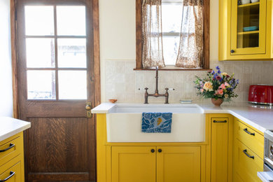 Inspiration for a small timeless u-shaped medium tone wood floor and brown floor enclosed kitchen remodel in Philadelphia with a farmhouse sink, glass-front cabinets, yellow cabinets, quartz countertops, white backsplash, ceramic backsplash, stainless steel appliances, no island and white countertops