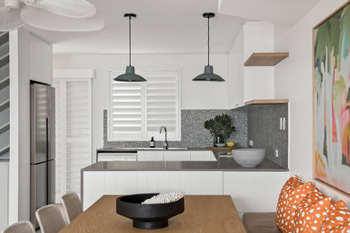 Design ideas for a contemporary u-shaped eat-in kitchen in Sunshine Coast with an integrated sink, flat-panel cabinets, white cabinets, grey splashback, stainless steel appliances, a peninsula and grey benchtop.