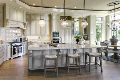 Example of a large classic l-shaped medium tone wood floor and brown floor eat-in kitchen design in Portland with raised-panel cabinets, white cabinets, quartz countertops, white backsplash, ceramic backsplash, paneled appliances, an island and multicolored countertops