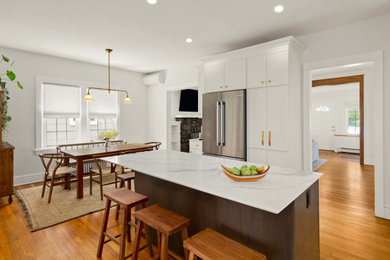 Photo of a mid-sized transitional l-shaped kitchen in New York with an undermount sink, recessed-panel cabinets, medium wood cabinets, quartz benchtops, white splashback, engineered quartz splashback, stainless steel appliances, medium hardwood floors, with island, brown floor and white benchtop.