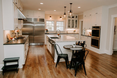 Design ideas for a large country u-shaped open plan kitchen in Atlanta with an undermount sink, shaker cabinets, white cabinets, granite benchtops, white splashback, subway tile splashback, stainless steel appliances, medium hardwood floors, with island, brown floor and black benchtop.