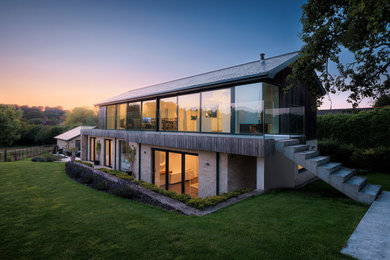 Photo of a large and brown contemporary two floor side detached house in Wiltshire with wood cladding, a pitched roof, a tiled roof, a grey roof and board and batten cladding.