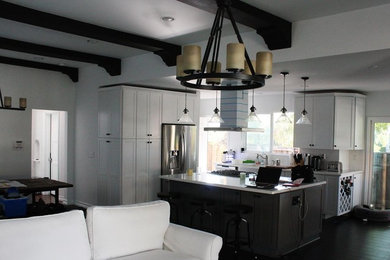 Open concept kitchen - mid-sized transitional l-shaped dark wood floor and brown floor open concept kitchen idea in Orange County with a farmhouse sink, recessed-panel cabinets, white cabinets, stainless steel appliances and an island