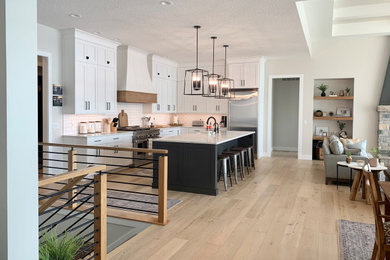 Inspiration for a large transitional l-shaped light wood floor, brown floor and tray ceiling open concept kitchen remodel in Other with a farmhouse sink, flat-panel cabinets, white cabinets, quartz countertops, white backsplash, porcelain backsplash, stainless steel appliances, an island and white countertops