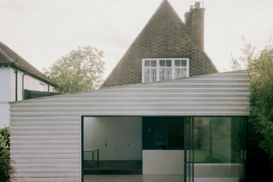 Photo of a large contemporary two-storey white house exterior in London with wood siding, a clipped gable roof, a mixed roof, a grey roof and board and batten siding.
