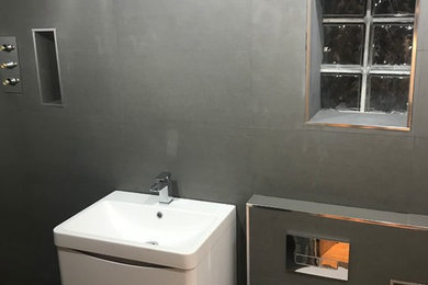 Small modern family bathroom in London with a wall mounted toilet, grey tiles, porcelain tiles, grey walls, porcelain flooring, a wall-mounted sink, tiled worktops, grey floors, grey worktops and white cabinets.