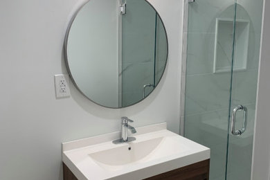 Bathroom - mid-sized gray tile brown floor and single-sink bathroom idea in Toronto with brown cabinets, white walls, an integrated sink, a hinged shower door, white countertops, a niche and a built-in vanity