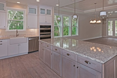 Open concept kitchen - mid-sized transitional l-shaped porcelain tile and beige floor open concept kitchen idea in Jacksonville with a farmhouse sink, shaker cabinets, white cabinets, granite countertops, beige backsplash, subway tile backsplash, stainless steel appliances and an island