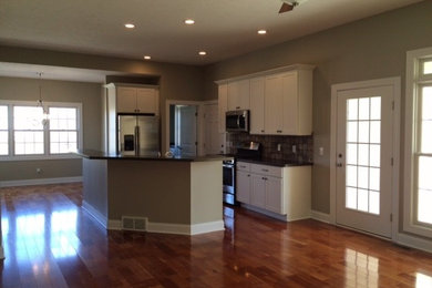 Open concept kitchen - large traditional galley dark wood floor and brown floor open concept kitchen idea in Cleveland with an undermount sink, shaker cabinets, white cabinets, quartz countertops, beige backsplash, stone tile backsplash, stainless steel appliances and an island