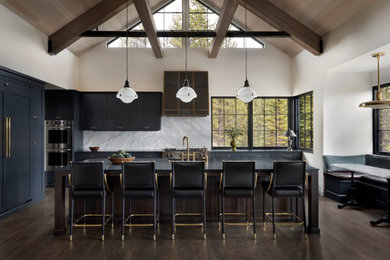 Huge mountain style single-wall medium tone wood floor, brown floor and exposed beam eat-in kitchen photo in Other with an integrated sink, shaker cabinets, soapstone countertops, white backsplash, marble backsplash, paneled appliances, an island and black countertops