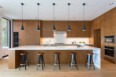 Foto de cocina contemporánea grande con fregadero bajoencimera, armarios con paneles lisos, puertas de armario de madera oscura, encimera de cuarzo compacto, salpicadero blanco, suelo de madera en tonos medios, una isla, encimeras blancas y suelo marrón