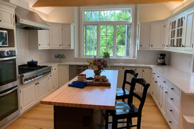 Inspiration for a cottage u-shaped light wood floor and brown floor kitchen remodel in Boston with an undermount sink, raised-panel cabinets, white cabinets, quartz countertops, white backsplash, ceramic backsplash, stainless steel appliances, an island and white countertops
