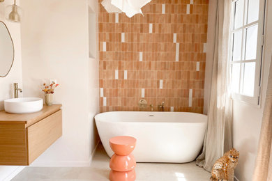 Cette image montre une salle d'eau méditerranéenne de taille moyenne avec une baignoire posée, des carreaux de céramique, un plan de toilette en bois, meuble simple vasque, sol en béton ciré, meuble-lavabo encastré et un mur en pierre.