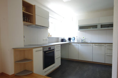 Geschlossene, Mittelgroße Moderne Küche ohne Insel in L-Form mit Einbauwaschbecken, flächenbündigen Schrankfronten, weißen Schränken, Mineralwerkstoff-Arbeitsplatte, Küchenrückwand in Weiß, Glasrückwand, Küchengeräten aus Edelstahl, Linoleum und grauem Boden in Frankfurt am Main