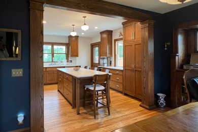 Mid-sized arts and crafts l-shaped light wood floor eat-in kitchen photo in Minneapolis with a single-bowl sink, shaker cabinets, medium tone wood cabinets, quartz countertops, white backsplash, subway tile backsplash, stainless steel appliances, an island and white countertops
