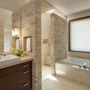 Cette image montre une salle de bain principale design avec une vasque, un placard à porte plane, des portes de placard en bois sombre, un plan de toilette en marbre, une douche d'angle, un WC à poser, un sol en travertin et une baignoire posée.