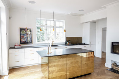 Photo of a large contemporary galley eat-in kitchen in Copenhagen with a drop-in sink, flat-panel cabinets, white cabinets, granite benchtops, metallic splashback, light hardwood floors, with island and glass sheet splashback.