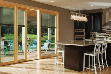 Large trendy single-wall light wood floor eat-in kitchen photo in Austin with flat-panel cabinets, black cabinets, multicolored backsplash, matchstick tile backsplash, stainless steel appliances and an island