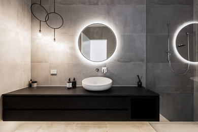 Design ideas for a mid-sized modern 3/4 wet room bathroom in Melbourne with flat-panel cabinets, black cabinets, a wall-mount toilet, gray tile, porcelain tile, grey walls, porcelain floors, a vessel sink, solid surface benchtops, grey floor, an open shower, black benchtops, a single vanity and a floating vanity.