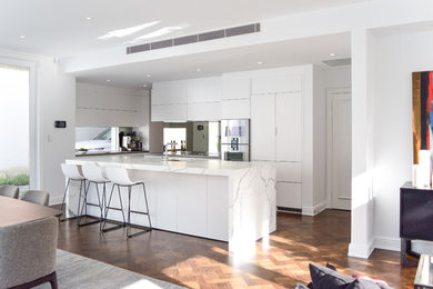 Inspiration for an expansive contemporary galley open plan kitchen in Melbourne with an undermount sink, flat-panel cabinets, white cabinets, marble benchtops, metallic splashback, mirror splashback, stainless steel appliances, medium hardwood floors and with island.