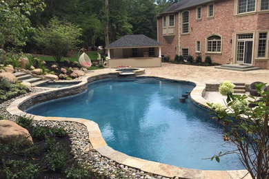 Large traditional backyard custom-shaped pool in New York with a hot tub and natural stone pavers.