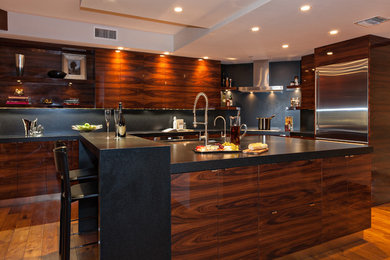 This is an example of a large contemporary l-shaped separate kitchen in Miami with an undermount sink, flat-panel cabinets, dark wood cabinets, granite benchtops, black splashback, stone slab splashback, stainless steel appliances, medium hardwood floors, with island, brown floor and black benchtop.