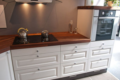 Inspiration for a mid-sized modern galley ceramic tile and gray floor eat-in kitchen remodel in Atlanta with raised-panel cabinets, dark wood cabinets, wood countertops, an island, brown countertops, a drop-in sink and white appliances