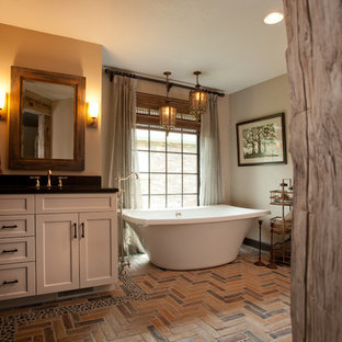 Idée de décoration pour une salle de bain principale chalet de taille moyenne avec un placard à porte shaker, des portes de placard blanches, une baignoire indépendante, un mur beige, un sol en brique et un lavabo encastré.