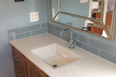 Inspiration for a mid-sized timeless 3/4 blue tile and glass tile ceramic tile and brown floor alcove shower remodel in Philadelphia with furniture-like cabinets, medium tone wood cabinets, a two-piece toilet, blue walls, an integrated sink, solid surface countertops, a hinged shower door and white countertops