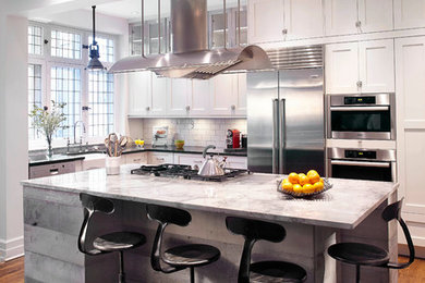 Eat-in kitchen - mid-sized industrial l-shaped medium tone wood floor eat-in kitchen idea in Montreal with a farmhouse sink, shaker cabinets, white cabinets, granite countertops, white backsplash, subway tile backsplash, stainless steel appliances and an island