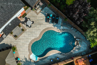 Diseño de piscina alargada exótica extra grande a medida en patio trasero con paisajismo de piscina y adoquines de hormigón