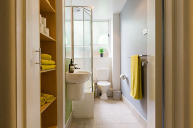 Small eclectic 3/4 bathroom in Melbourne with open cabinets, medium wood cabinets, a drop-in tub, a shower/bathtub combo, a two-piece toilet, green tile, ceramic tile, grey walls, cement tiles, a wall-mount sink, beige floor and a hinged shower door.