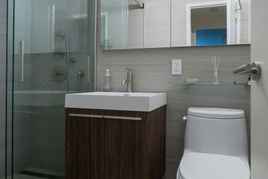 Photo of a small contemporary 3/4 wet room bathroom in New York with flat-panel cabinets, white cabinets, a one-piece toilet, gray tile, porcelain tile, grey walls, porcelain floors, an integrated sink, engineered quartz benchtops, grey floor and a sliding shower screen.