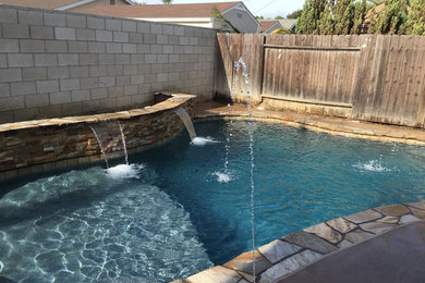 Mid-sized tropical backyard custom-shaped lap pool in Orange County with a hot tub and concrete slab.